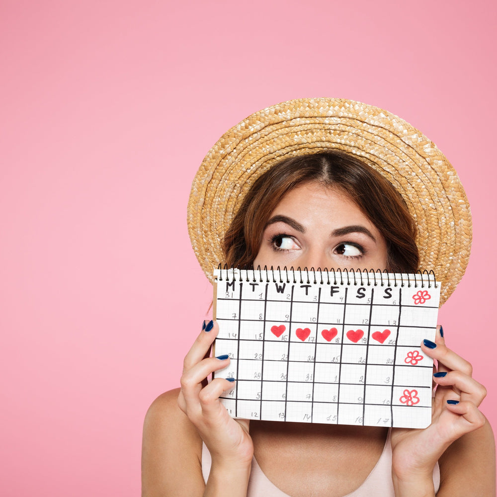 Frau mit Strohhut mit Periodenkalender in der Hand auf pinken Hintergrund 