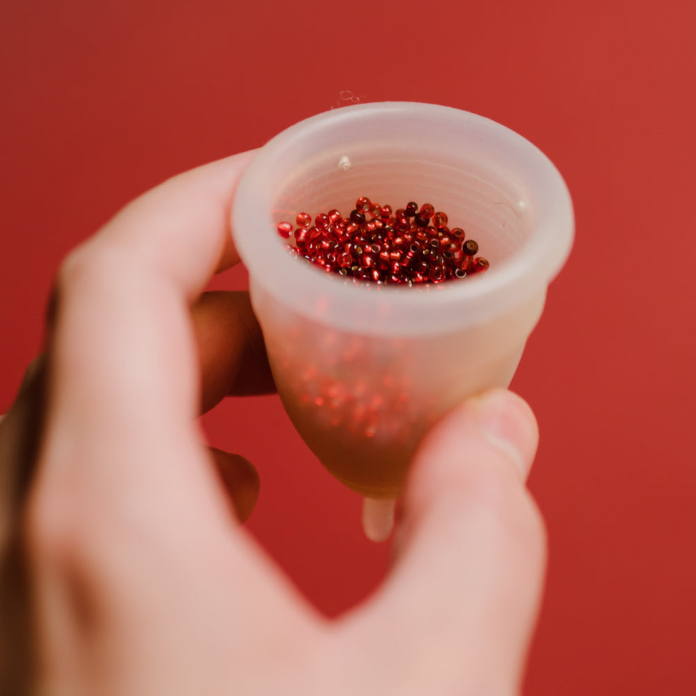 Periodentasse in Hand gefüllt mit roten Perlen auf roten Hintergrund 