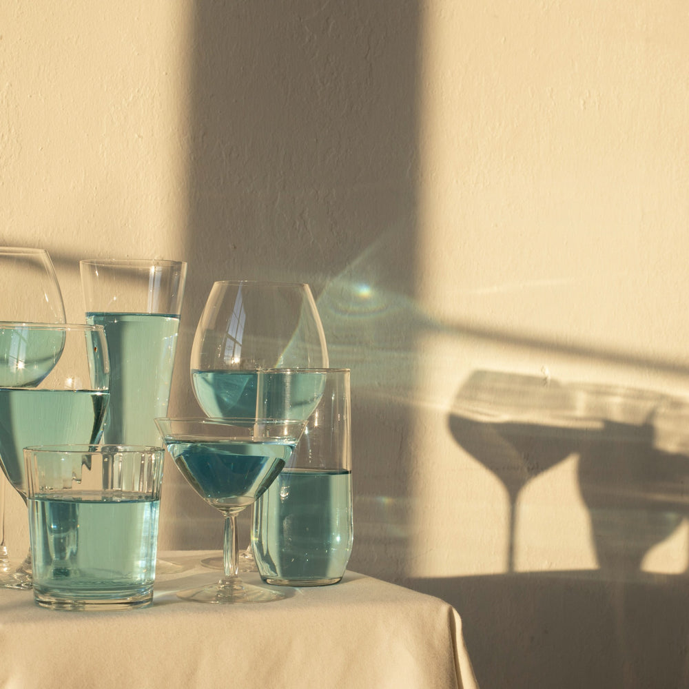 Gläser mit hellblauer durchsichtiger Flüssigkeit auf Tisch in Sonne mit Schatten auf gelblicher Wand 