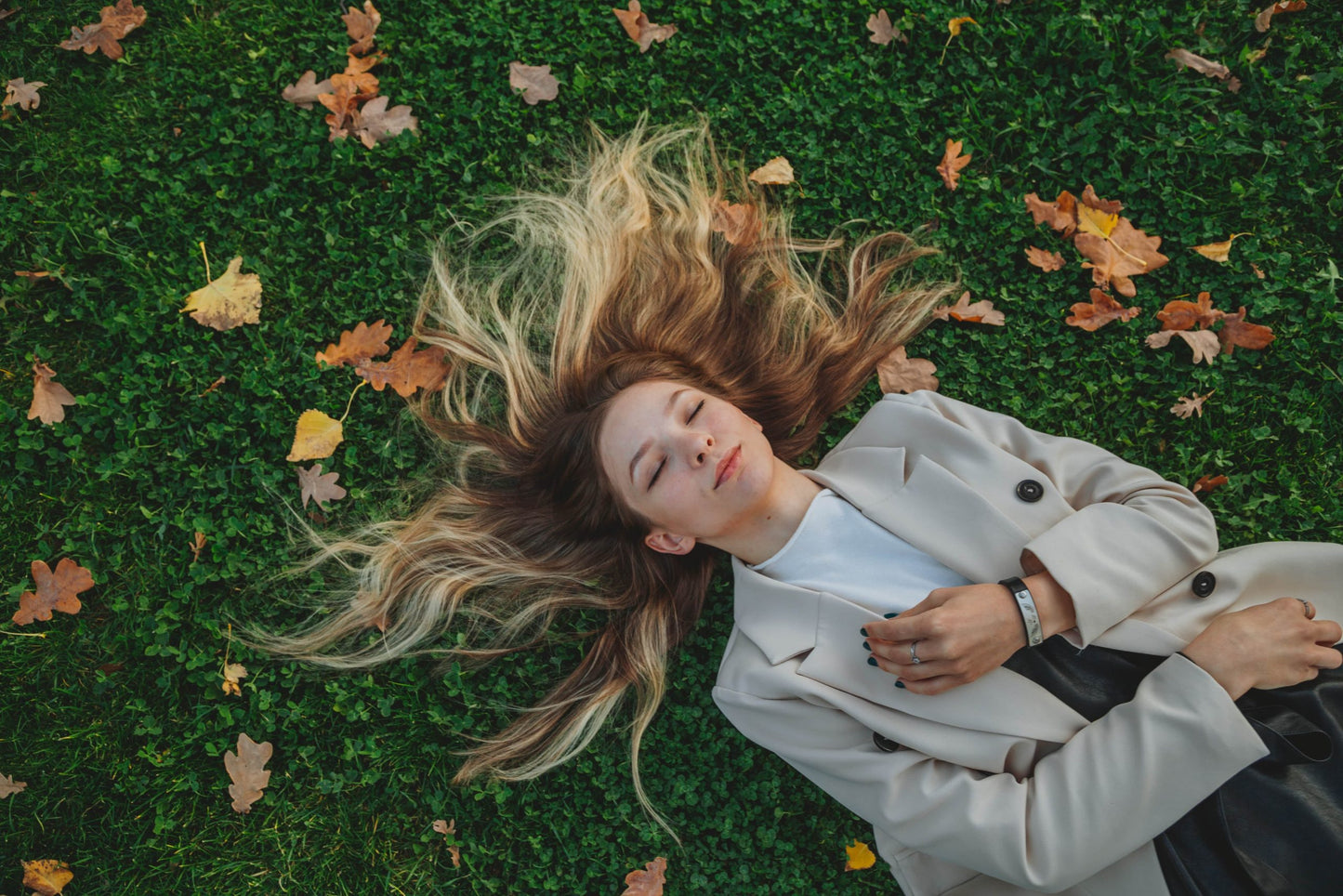 Blonde Frau liegt auf Gras mit Herbstblättern